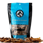 Bag of dried sardines with a blue label and black dog icon, surrounded by scattered sardines on a white background.