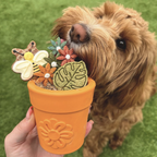 Dog sniffing a toy shaped like a flower pot with floral decorations on a grassy background
