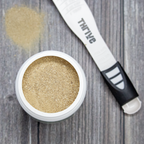 Small container of gold powder with a applicator on a wooden surface