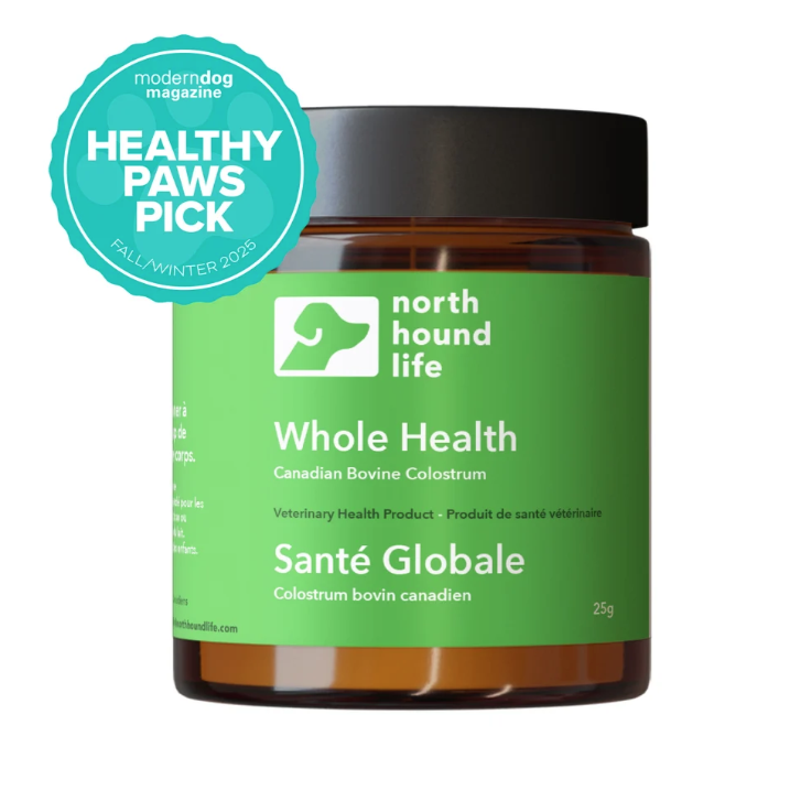 A jar of North Hound Life Whole Health Canadian Bovine Colostrum dog supplement, featuring a green label and black lid, with a teal Modern Dog Magazine Healthy Paws Pick badge on a white background.